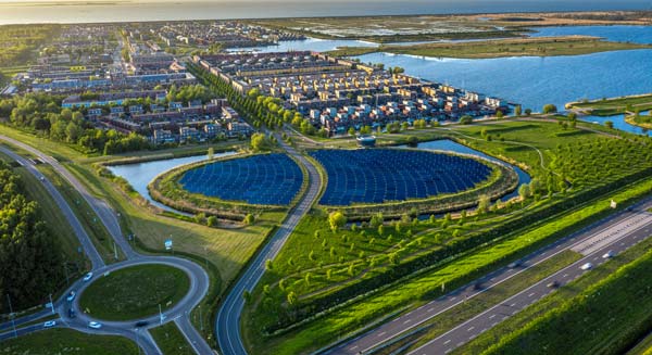 Aerial view of a sustainable landscape featuring large circular solar panel arrays surrounded by greenery, with nearby residential neighborhoods, waterways, and roads, illustrating renewable energy integration in urban planning.