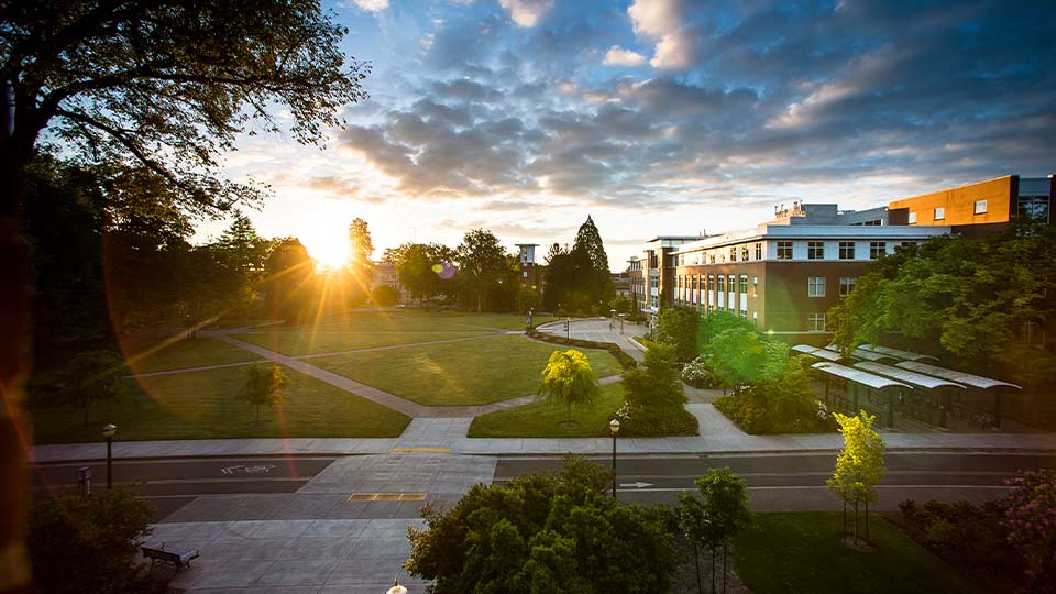 A bright sun rises over distant trees on the quad in front of Oregon State University's Valley Library.