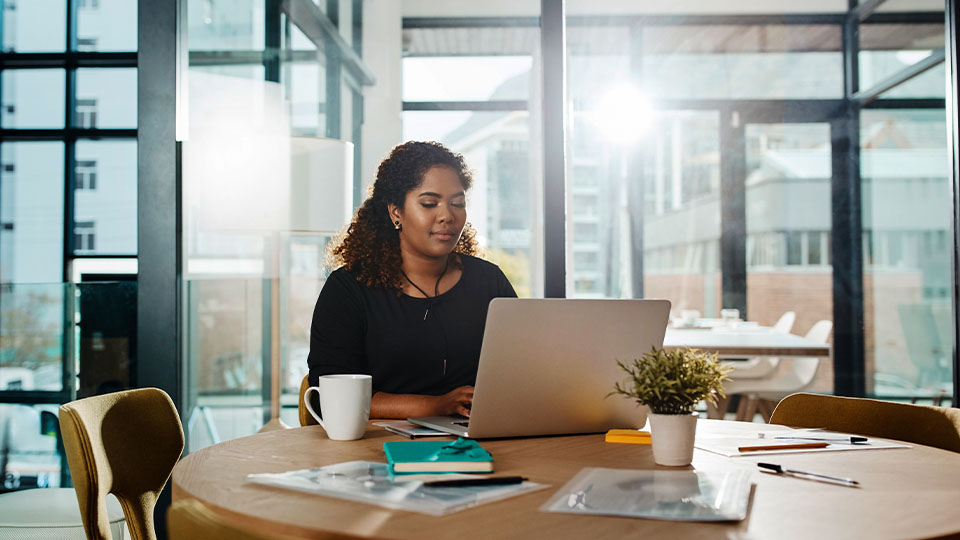 A woman working on a laptop at a round table in a modern, sunlit office