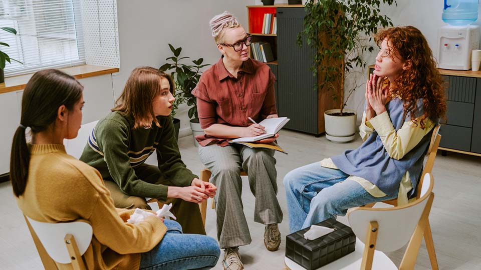 People participating in a group counseling session in a light-filled space with plants.