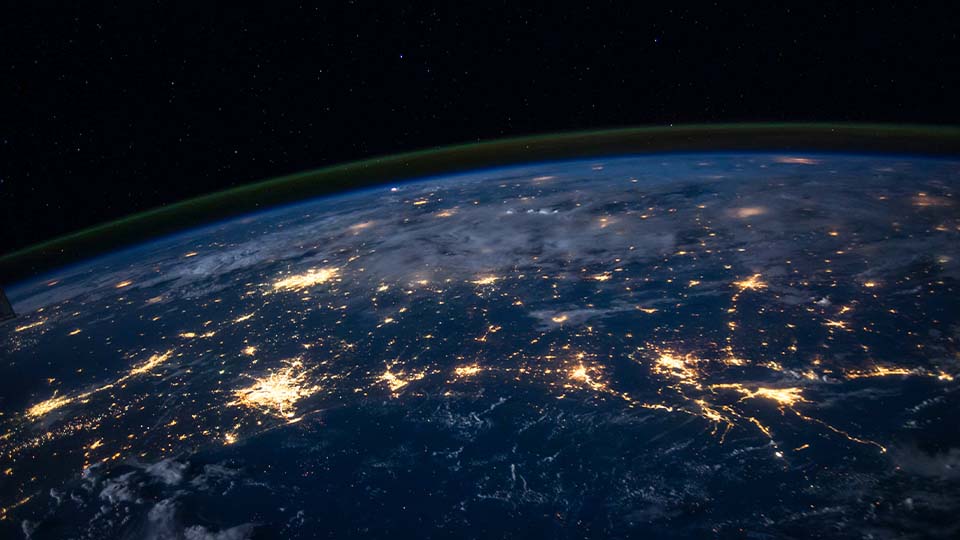 A curved view of Earth and its atmosphere from space at night, showing city lights, clouds, and stars