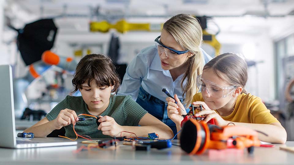 Teacher guiding students in a project that involves screwdrivers and wires. The students are concentrating on their work, and the teacher is talking to them.