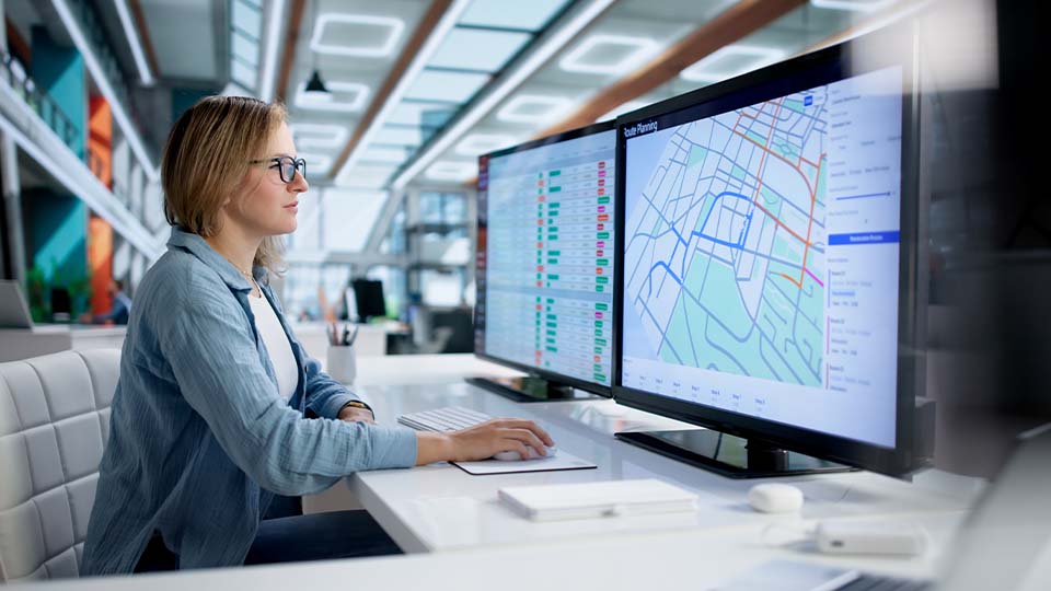 Person reviewing route maps and operational data on dual monitors at a workstation.