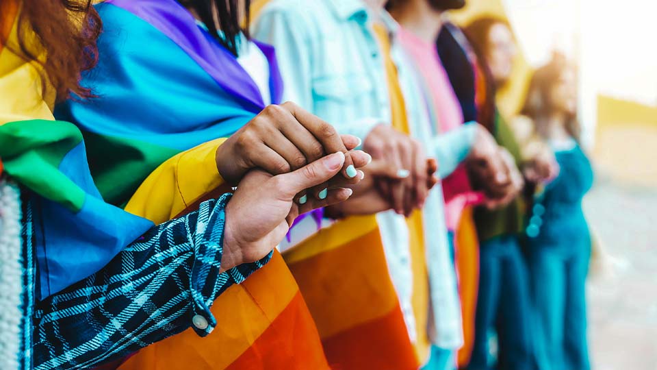 People of all races and genders holding hands with rainbow blankets symbolizing diversity and connection.