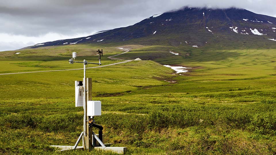 Remote weather station collecting environmental data in a vast green landscape with a mountain in the distance.