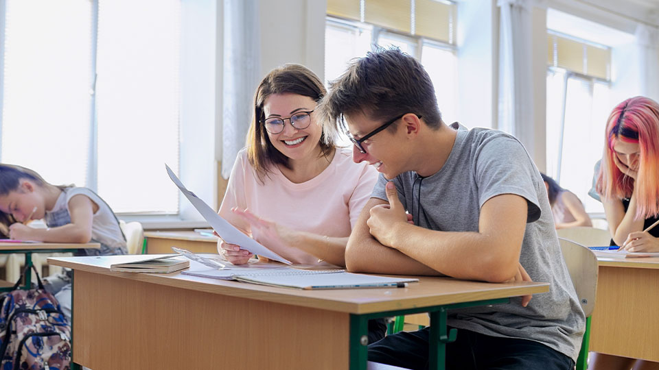 Teacher supports student one-on-one in a bright classroom, reflecting inclusive, student-centered learning strategies.