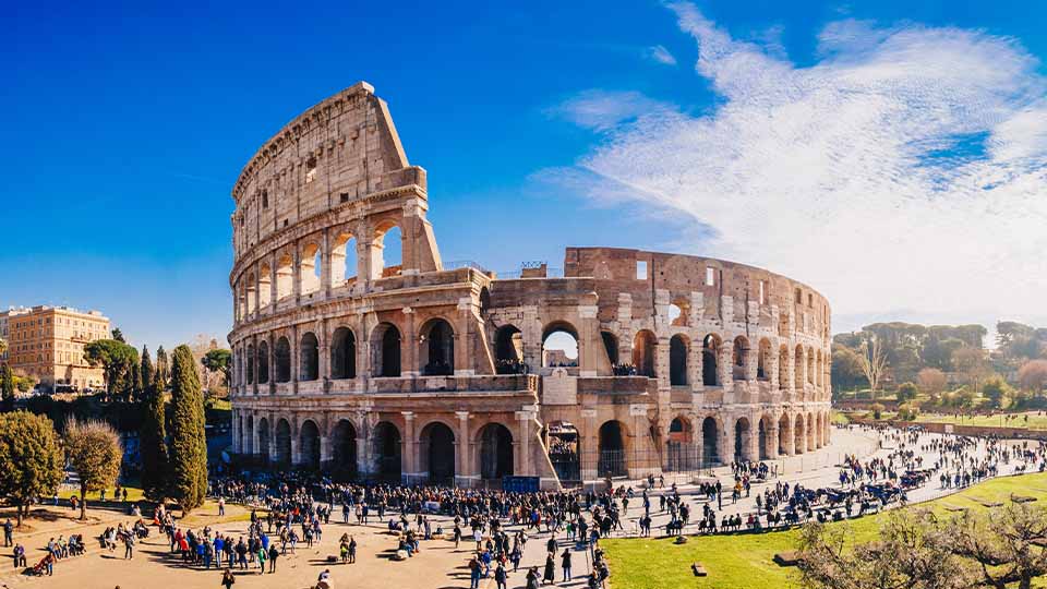 The Colosseum in Rome, Italy, shown under a bright blue sky with scattered clouds.