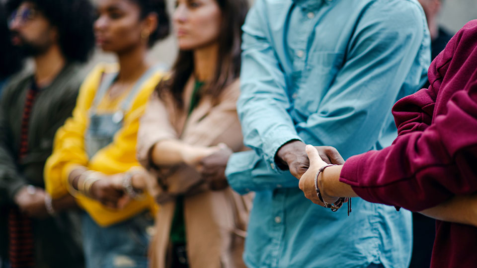 People from different races and genders linking hands over crossed arms