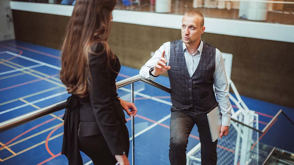 Business professionals having a discussion on a staircase overlooking a sports gymnasium with blue flooring